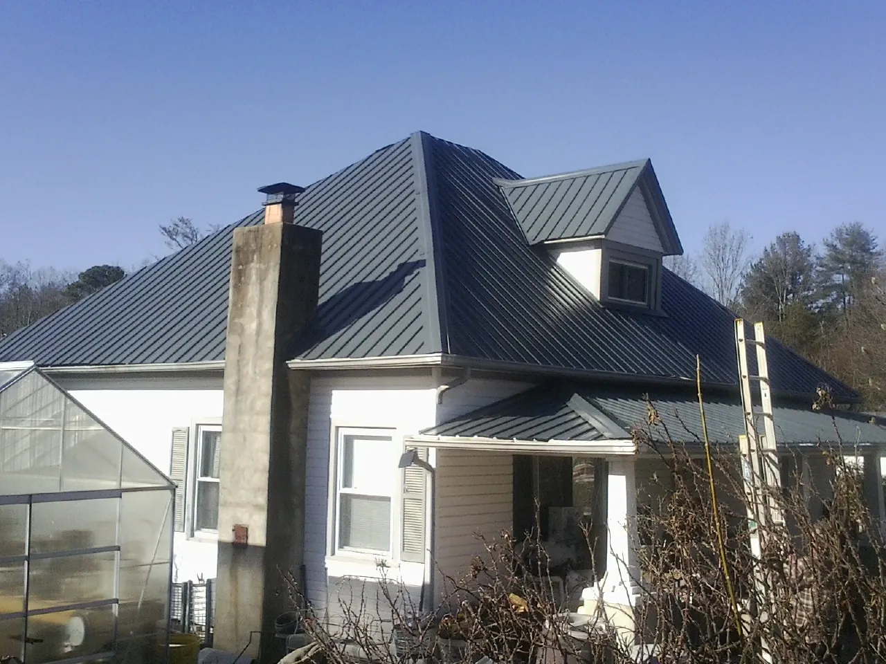 Dark blue standing seam metal roof on a white farmhouse with dormer — Slate & Tile Roof Repair by Roofing Brothers in Sharon Springs