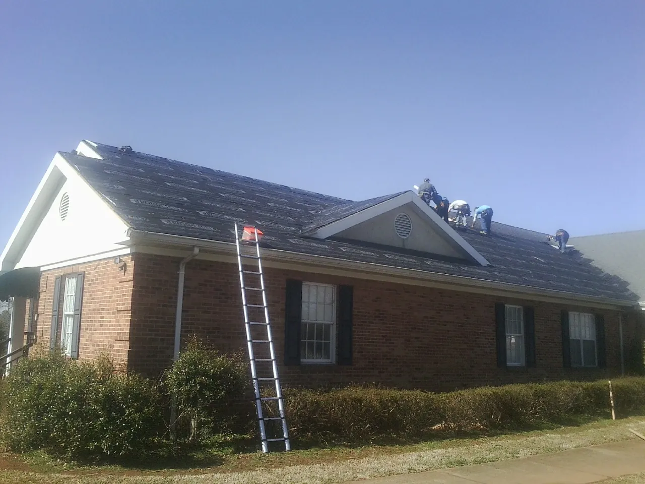Crew tearing shingles off a brick ranch roof with a ladder set — Metal Roof Repair work by our crew in Sharon Springs