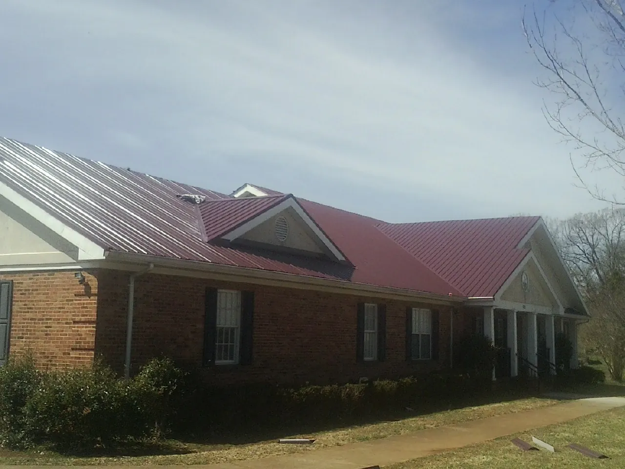 Red metal roof with gabled entries on a long brick building, from a Hail Damage Roof Repair job in Sharon Springs
