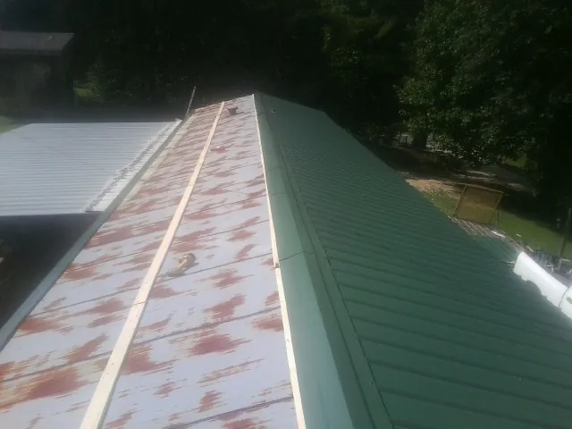 Old rusted panels beside newly installed green metal roofing — Wind Damage Roof Repair by Roofing Brothers in Sharon Springs