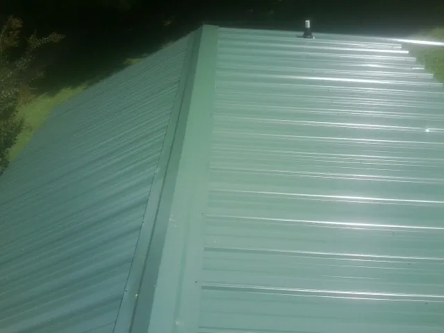 New green metal panels meeting at the ridge of a roof — Flat Roof Repair work by our crew in Sharon Springs