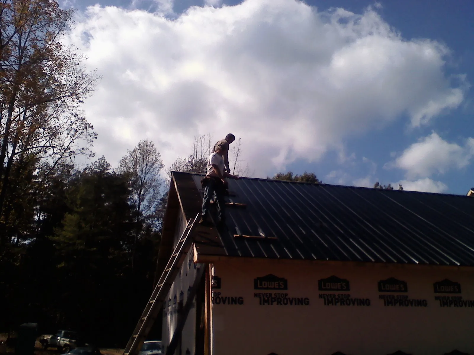 Roofer fastening dark metal panels high against a cloudy sky, from a Roof Inspection job in Sharon Springs
