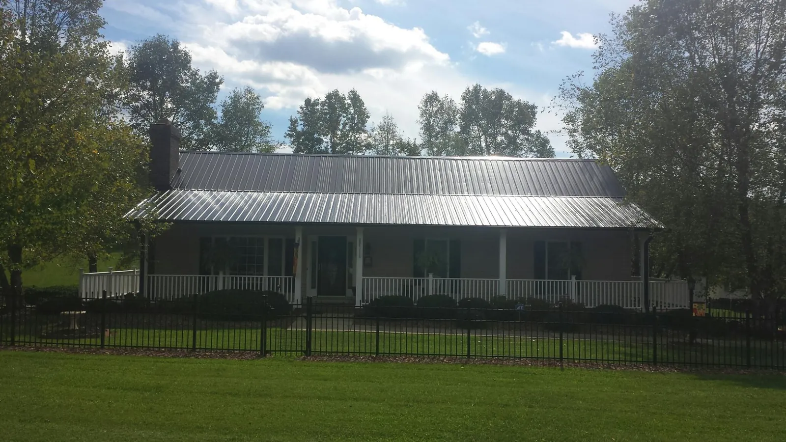 Gray metal roof on a brick ranch with a full width front porch — Gutter Guard Installation work by our crew in Sharon Springs