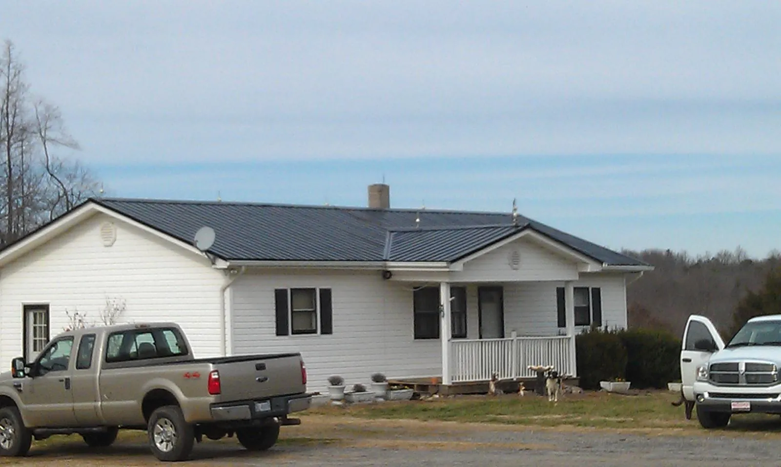 Finished dark metal roof on a white ranch home with work trucks parked in Sharon Springs