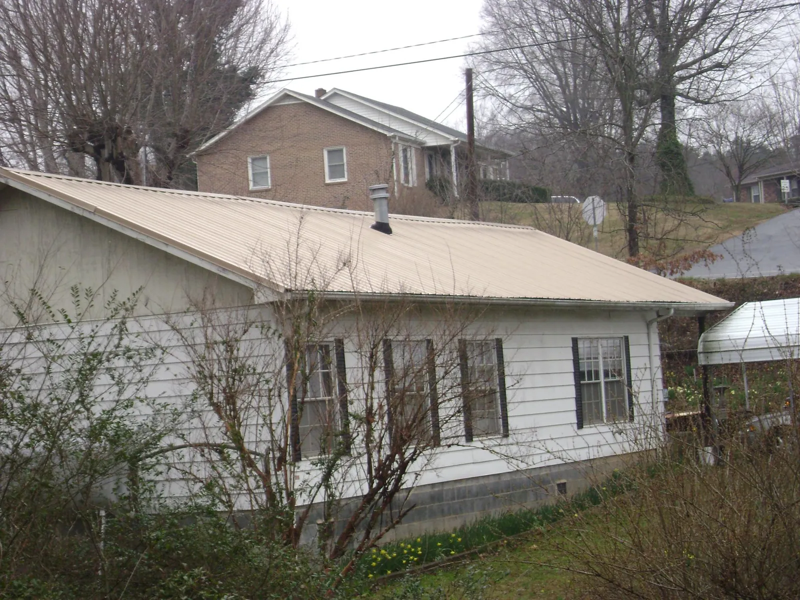Tan metal roof on a white sided house set into a hillside — Commercial Roofing by Roofing Brothers in Sharon Springs