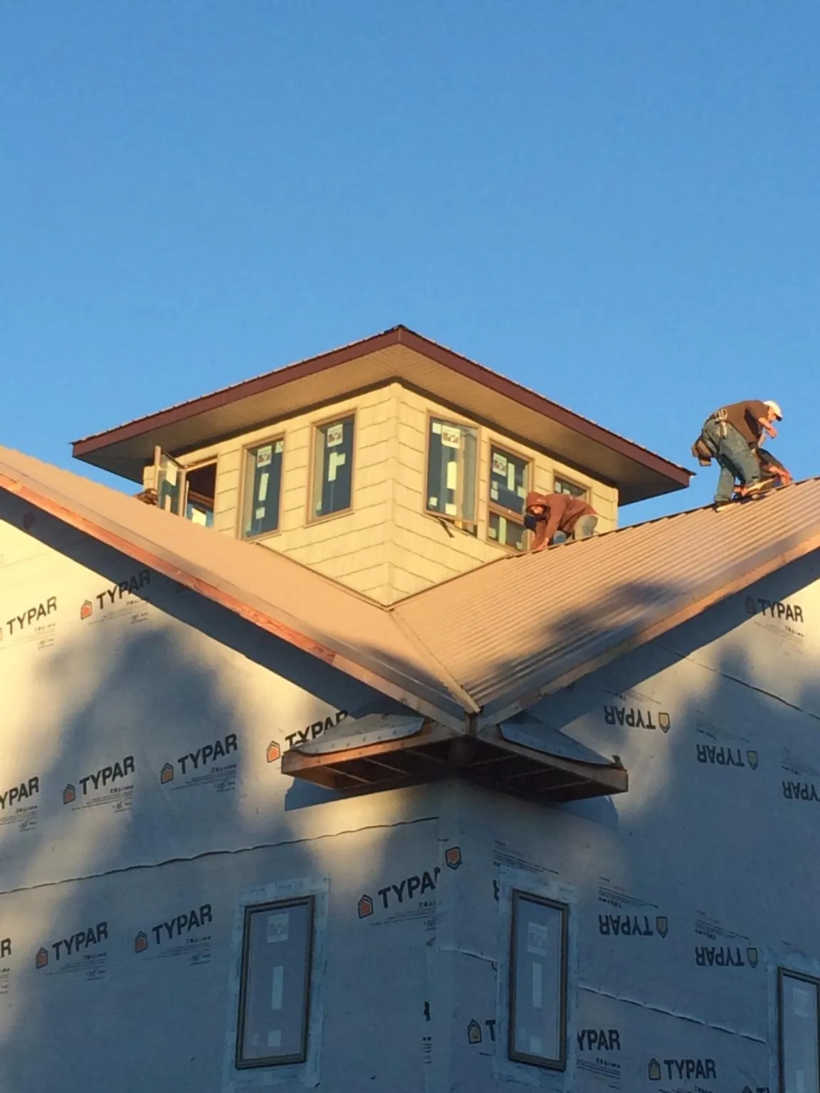 Roofers working around a rooftop cupola on a new metal roof at sunset — Roof Waterproofing in Sharon Springs by Roofing Brothers